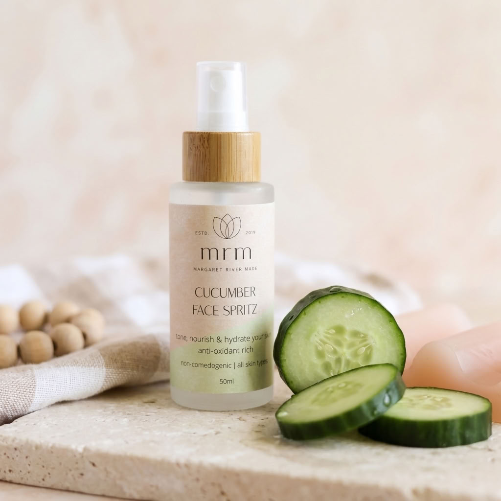 A 50ml bottle of MRM Cucumber Face Spritz with a bamboo cap, styled on a stone surface with cucumber slices, a folded towel, and a pink soap bar in the background.