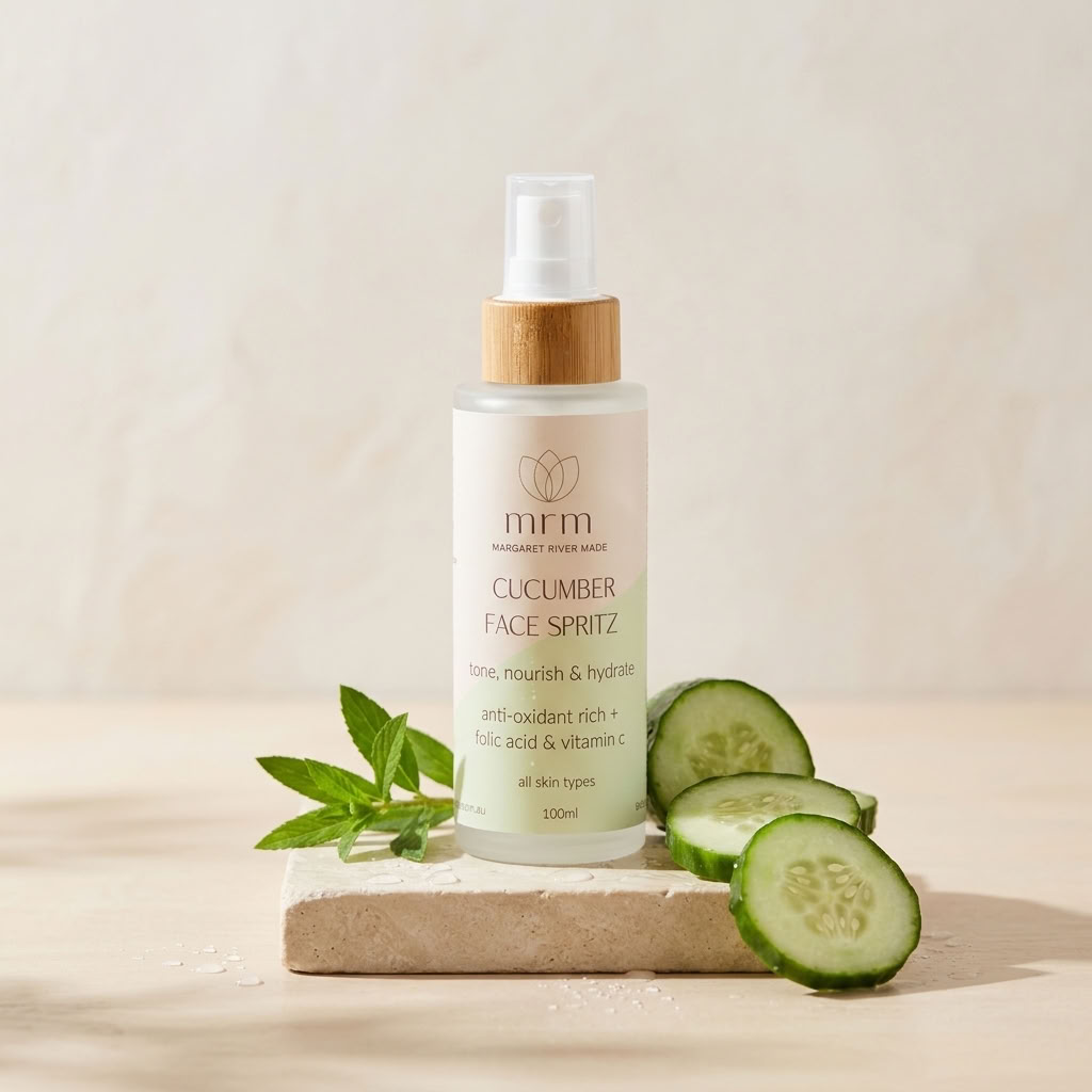 A 500ml bottle of MRM Cucumber Face Spritz with a bamboo cap, displayed on a stone block with fresh cucumber slices and mint leaves against a warm beige background.