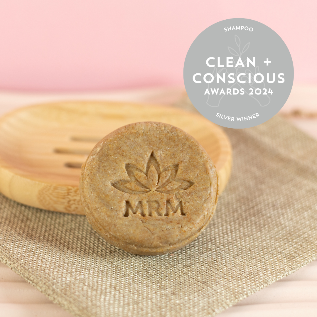 An Anti-Dandruff Shampoo Bar with an engraved logo, placed on a wooden comb with a beige background. There is a badge indicating &