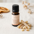 A small amber glass bottle of MRM Frankincense pure essential oil with a black cap, set on a textured cream linen surface with dried orange slices and incense sticks as props.