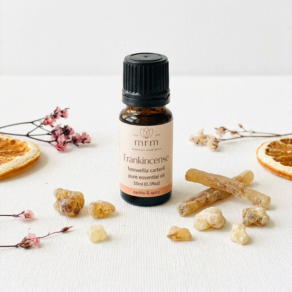 A 10ml bottle of mrm Frankincense pure essential oil, styled on a white textured fabric background with natural incense sticks, resin pieces, dried orange slices, and small pink flowers.