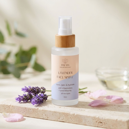 A 50ml bottle of MIMI Lavender Face Spray with a bamboo cap, styled on a stone slab with lavender sprigs and pink petals.