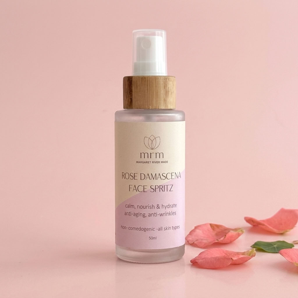 Margaret River Rocks Rose Damascena Face Spritz in a frosted glass bottle with a bamboo cap, set against a soft pink background with decorative rose petals.