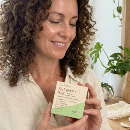 Woman holding a curly hair shampoo bar packaging with plants in the background