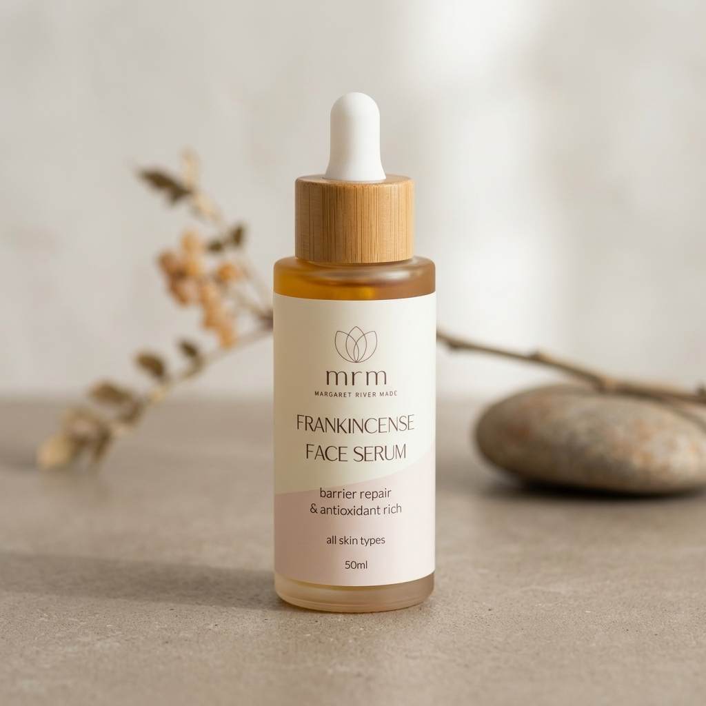 A 50ml bottle of MM Frankincense Face Serum with a bamboo dropper cap, set on a neutral textured surface with soft-focus dried flowers and a stone in the background.